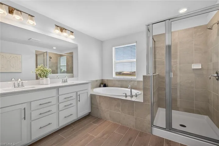 Bathroom featuring a double vanity with white cabinets and a large mirror, a separate shower enclosure with glass doors, and a built-in bathtub
