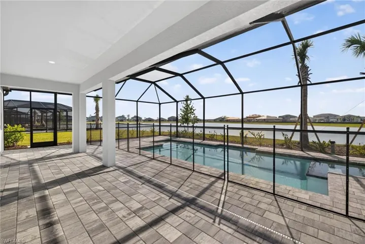 Expansive screened-in lanai with paver flooring, providing a covered patio area and a swimming pool with a safety fence, all overlooking a serene body of water