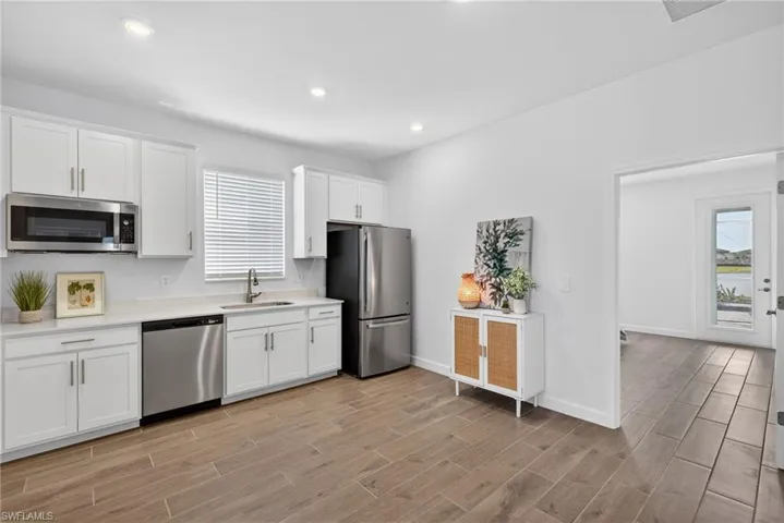 The kitchen features white cabinetry, stainless steel appliances, and wood-look tile flooring
