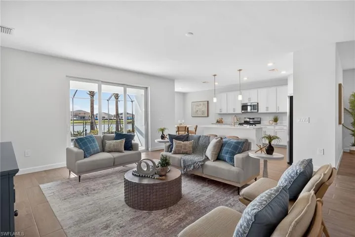 The living area features light wood-look flooring, white walls, and a large sliding glass door that opens to a screened patio with views of a body of water and other properties