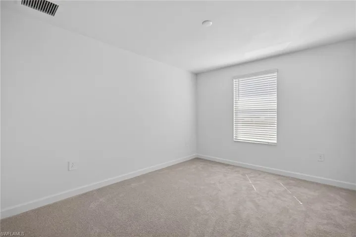 This room features neutral-toned carpeting, white walls, and a window with horizontal blinds