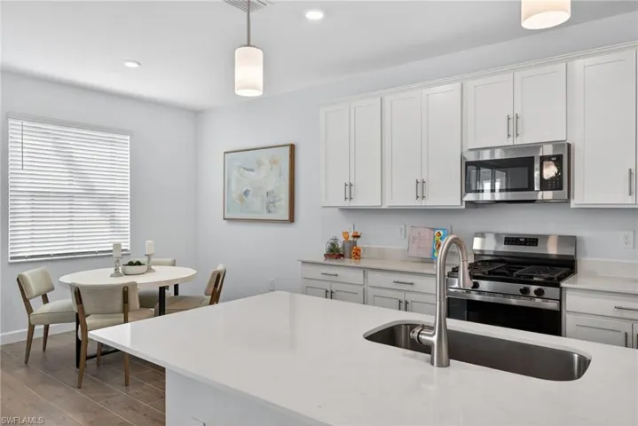 The kitchen features a large island with an undermount sink and a stainless steel faucet, white cabinetry, stainless steel appliances including a microwave and range, and light-colored countertops