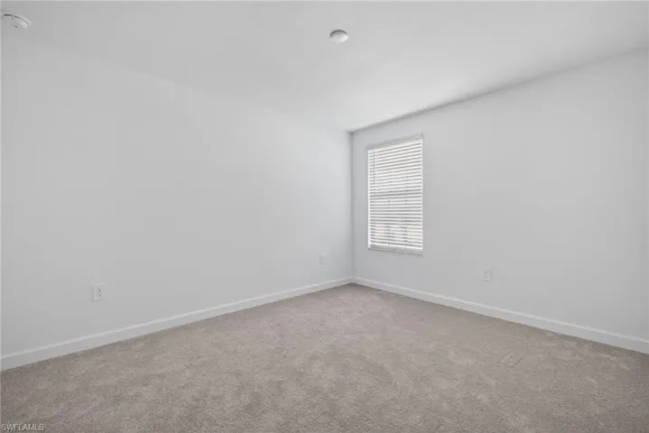 This room features light-colored walls, carpeted flooring, and a window with blinds, providing natural light
