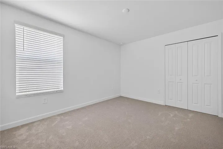 This room features light-colored carpet, a window with horizontal blinds, and a bi-fold closet door