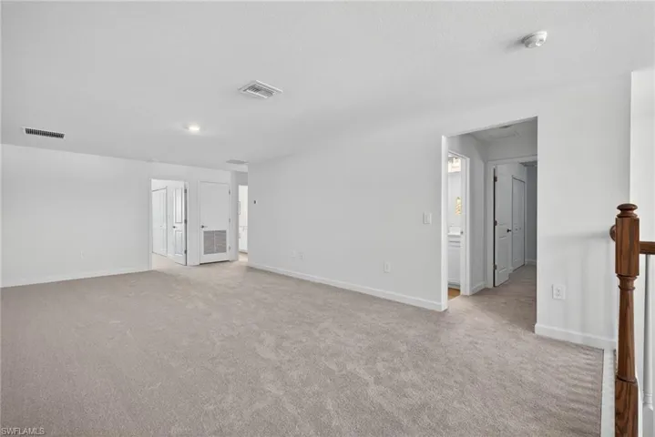 Spacious interior room with light-colored carpet, white walls, and recessed lighting