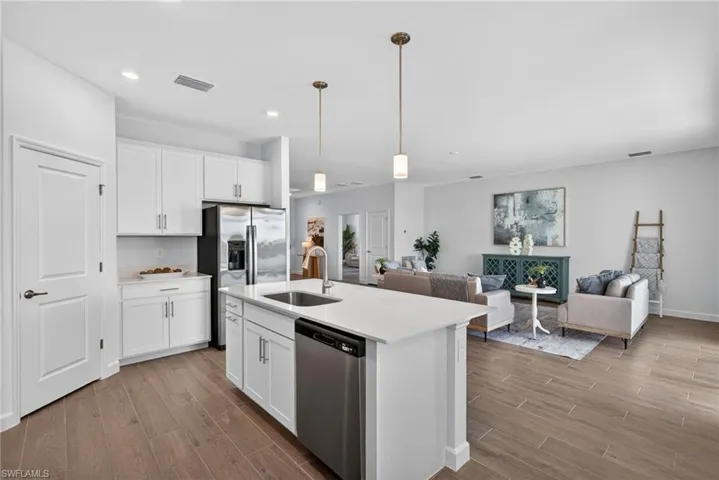 Open concept living area featuring a kitchen with white cabinetry, a stainless steel refrigerator, and a kitchen island with a sink and dishwasher