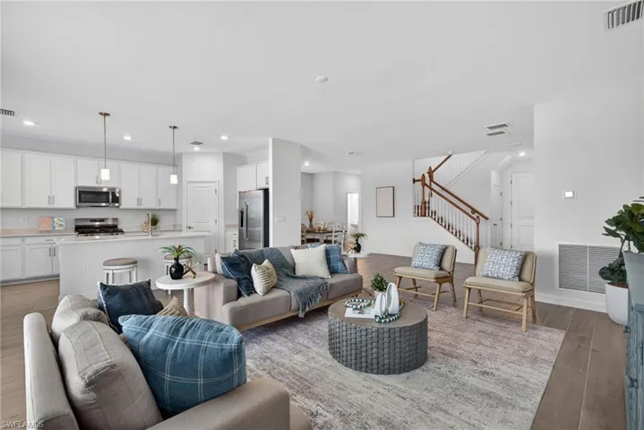 The property features an open living area with light wood flooring, a kitchen with white cabinetry and stainless steel appliances, and a staircase with wood banisters