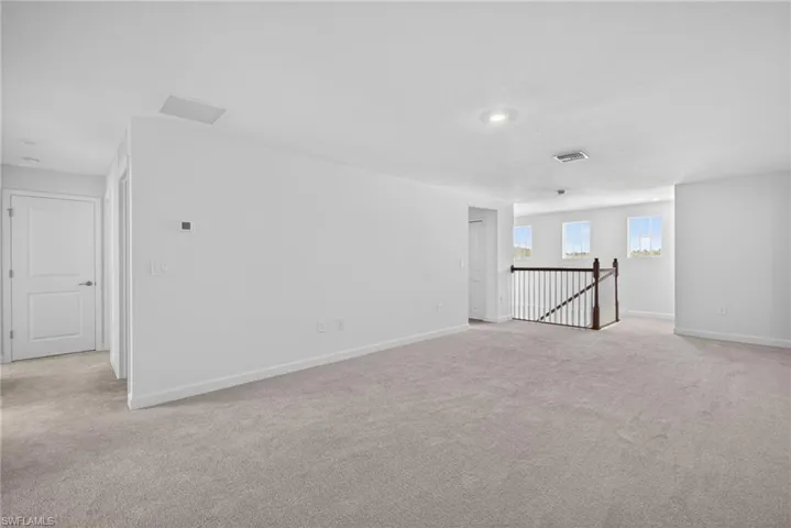 This spacious room features light-colored carpeting, white walls, and recessed lighting
