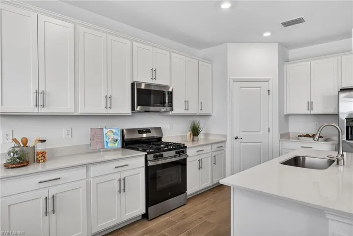 The kitchen features white cabinetry, stainless steel appliances, light-colored countertops, and wood-look flooring