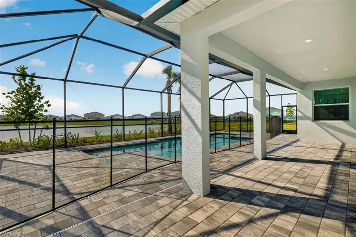 The property features a screened-in pool area with a paved deck, a safety fence around the pool, and an outdoor patio space with an overhead roof and structural columns