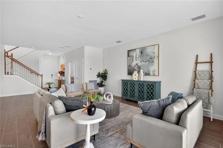 Spacious living area featuring light-toned walls, wood-look flooring, and a visible staircase with white railings and wood banisters