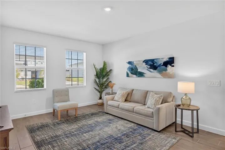 Spacious living area featuring light-colored walls, tile flooring, two windows with blinds, and recessed lighting