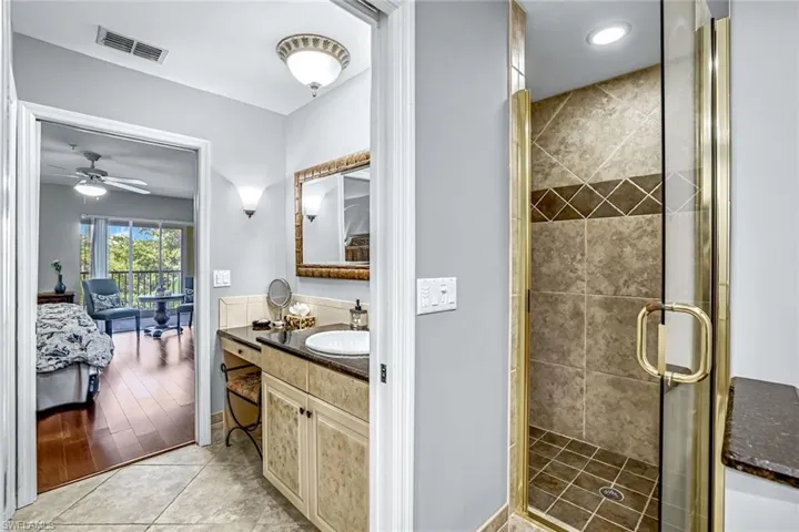 Ensuite bathroom featuring vanity, a shower stall, light tile patterned floors, and a ceiling fan