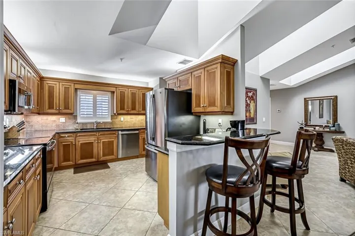 Kitchen with wood finish cabinetry, a kitchen bar, stainless steel appliances, light tile patterned floors, and lofted ceiling