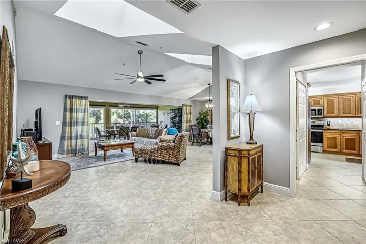 Living area featuring a skylight, light tile patterned flooring, ceiling fan, and vaulted ceiling
