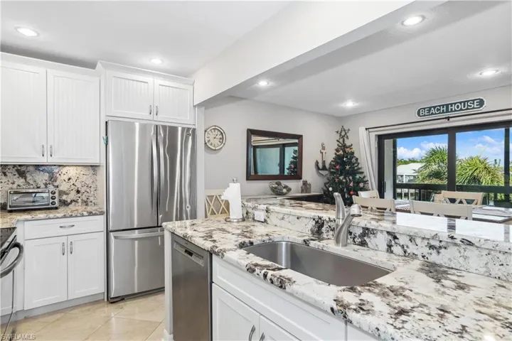 Kitchen with light stone counters, sink, white cabinets, and appliances with stainless steel finishes