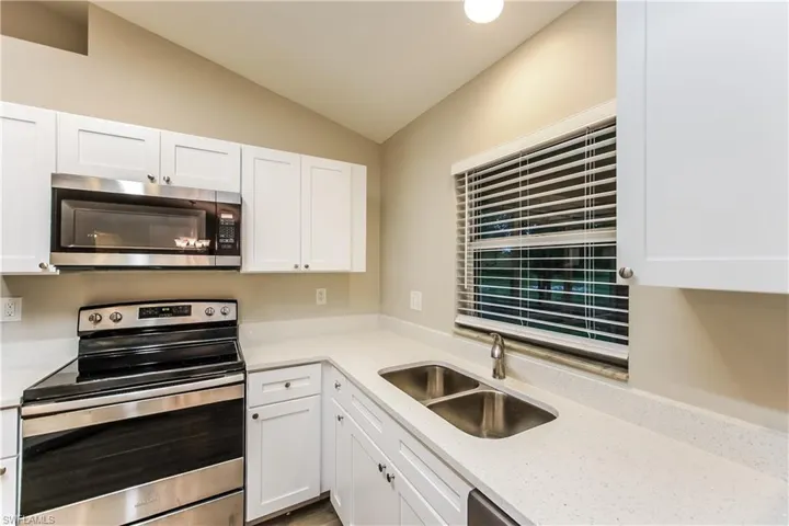 Kitchen with appliances with stainless steel finishes, white cabinetry, light stone counters, and lofted ceiling