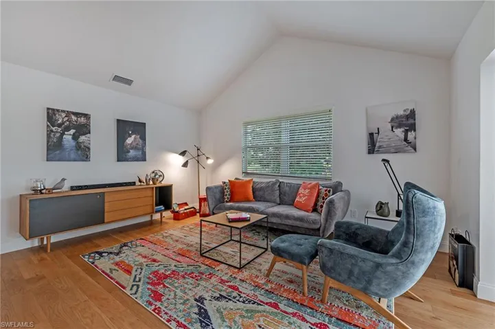 Living room featuring high vaulted ceiling, visible vents, and wood finished floors