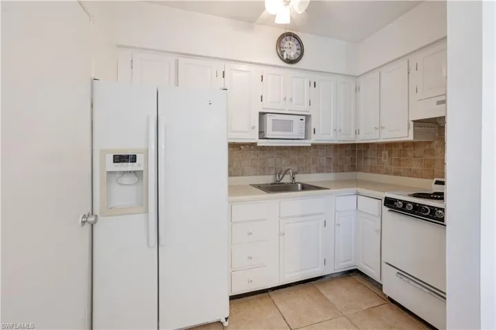 Kitchen featuring white appliances, light countertops, white cabinetry, and decorative backsplash
