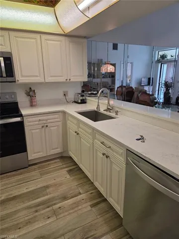 Kitchen featuring stainless steel appliances, light stone counters, open floor plan, light wood-style flooring, and lofted ceiling