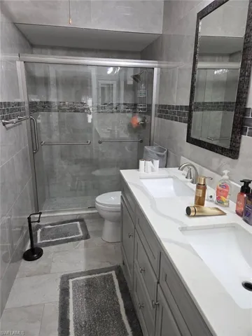 Bathroom with double vanity, a stall shower, and tile walls