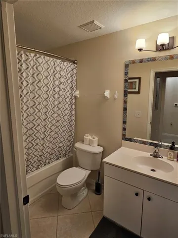 Bathroom with vanity, shower / tub combo, dark tile patterned flooring, and a textured ceiling