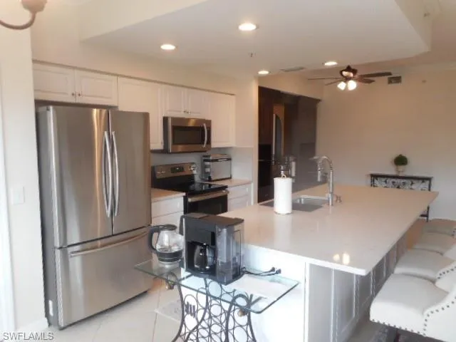 Kitchen with appliances with stainless steel finishes, white cabinets, a breakfast bar, a ceiling fan, and light tile patterned floors