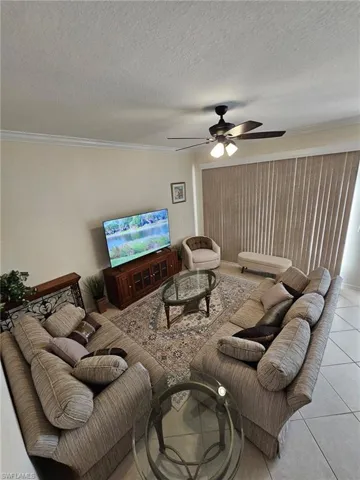 Tiled living area with a ceiling fan, a textured ceiling, and ornamental molding