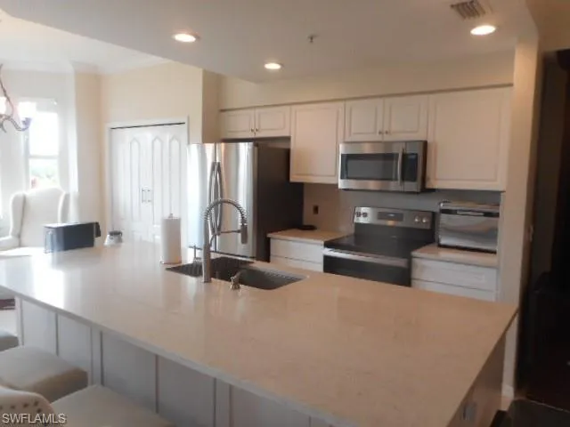 Kitchen with appliances with stainless steel finishes, recessed lighting, a breakfast bar area, white cabinetry, and light stone countertops