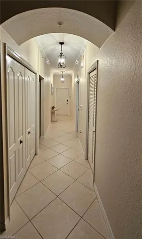 Corridor featuring a textured wall, light tile patterned floors, crown molding, and arched walkways