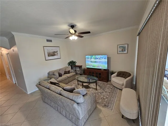 Living room with light tile patterned flooring, crown molding, a ceiling fan, and a textured ceiling