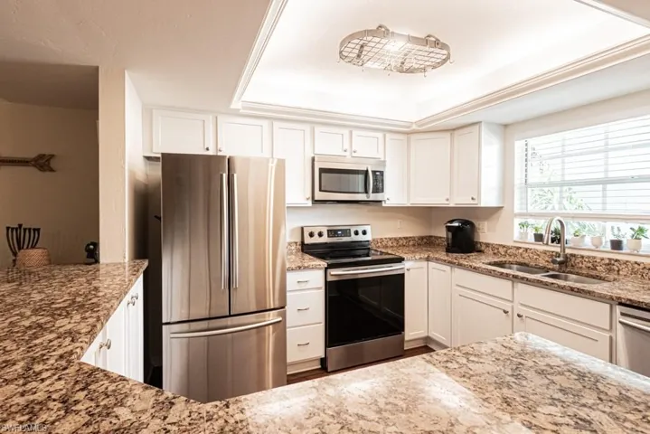 Kitchen featuring a tray ceiling, a sink, light stone countertops, appliances with stainless steel finishes, and white cabinets