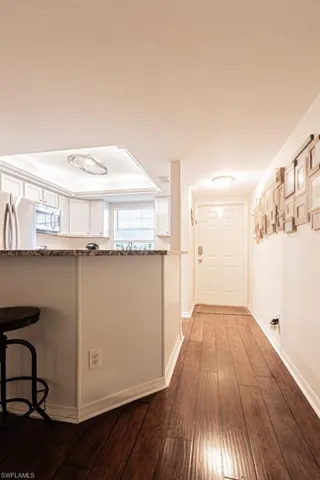 Hallway with wood-type flooring, a raised ceiling, a sink, and baseboards