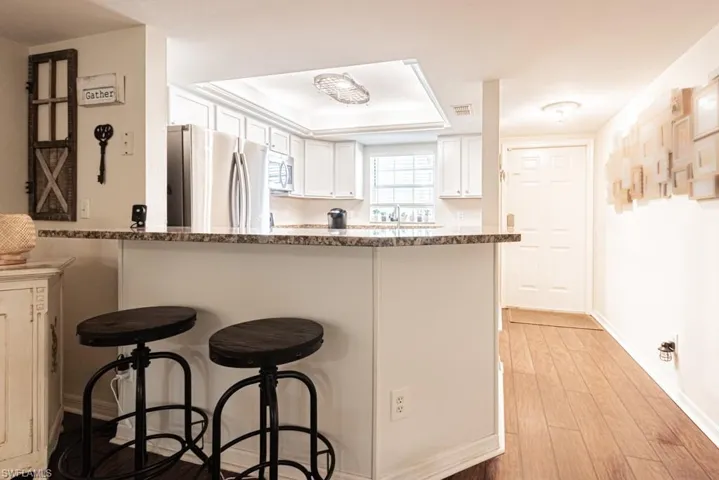 Kitchen with a kitchen breakfast bar, light wood-type flooring, white cabinets, a peninsula, and appliances with stainless steel finishes