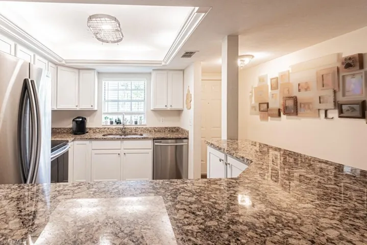 Kitchen with a sink, appliances with stainless steel finishes, light stone counters, and visible vents