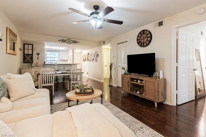 Living room with baseboards, dark wood-style flooring, visible vents, and a ceiling fan