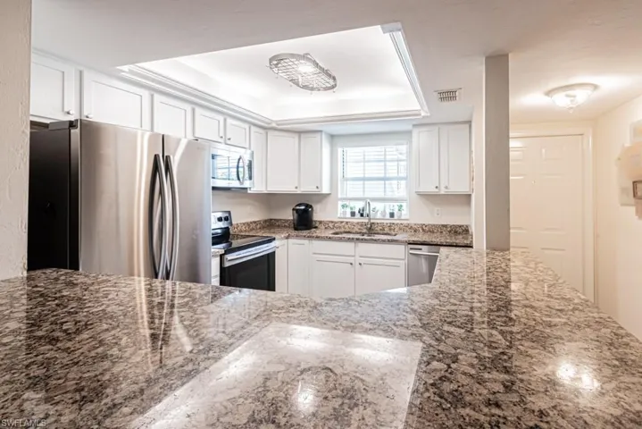 Kitchen featuring a tray ceiling, stainless steel appliances, dark stone countertops, a sink, and visible vents