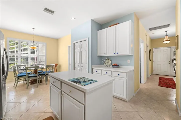 Kitchen with decorative light fixtures, white cabinetry, light countertops, a center island, and stainless steel refrigerator with ice dispenser