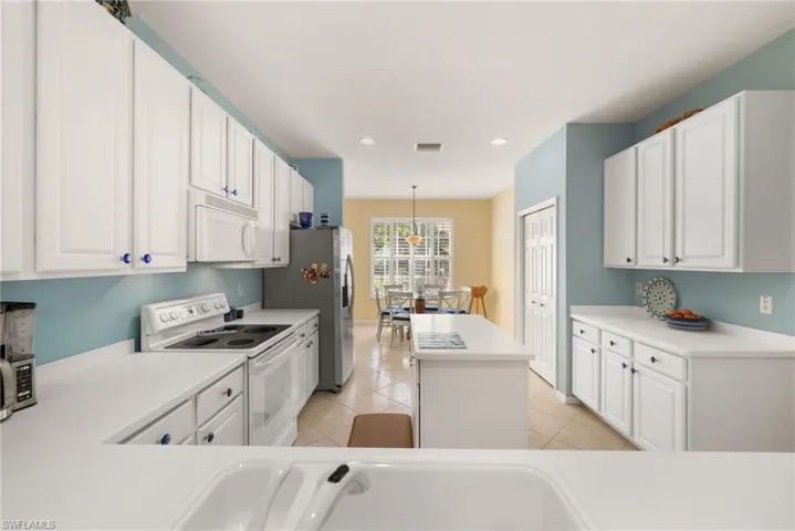 Kitchen with white appliances, white cabinets, light countertops, pendant lighting, and a center island