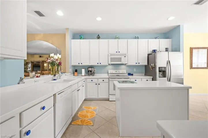 Kitchen featuring a kitchen island, white appliances, light countertops, and white cabinets