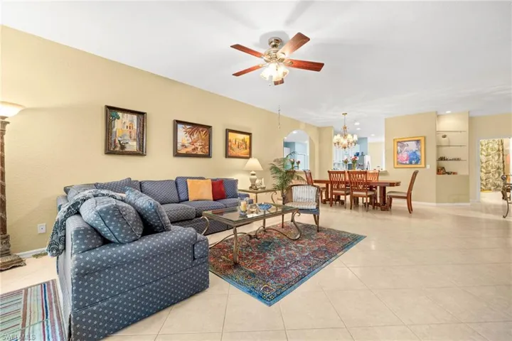 Living room featuring arched walkways, ceiling fan, light tile patterned floors, and hanging lights