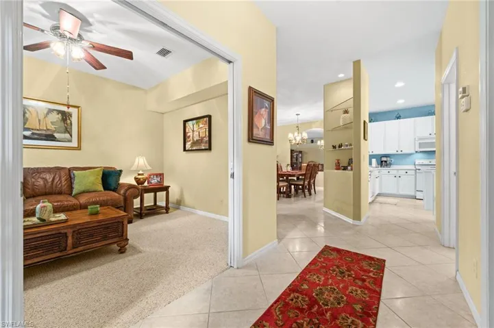 Living area with ceiling fan, light carpet, a chandelier, and light tile patterned flooring