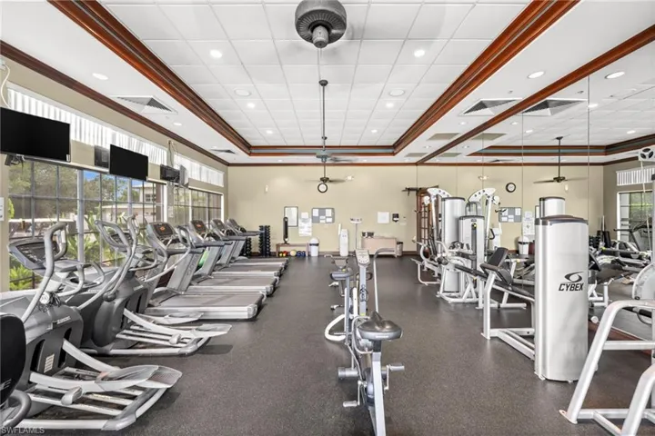 Exercise room with a tray ceiling, ornamental molding, recessed lighting, and a ceiling fan