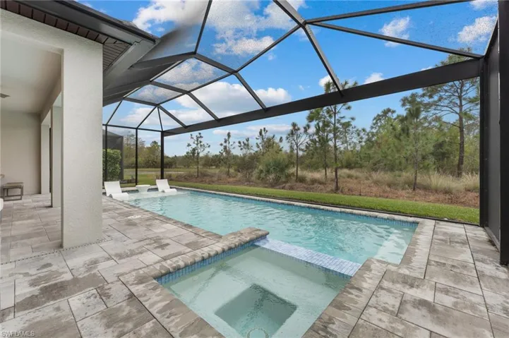 View of swimming pool featuring a patio area, glass enclosure, and an in ground hot tub