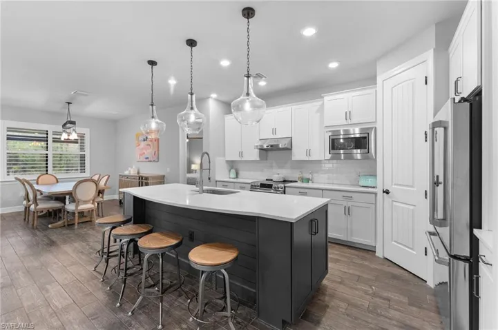 Kitchen with pendant lighting, appliances with stainless steel finishes, an island with sink, and white cabinets
