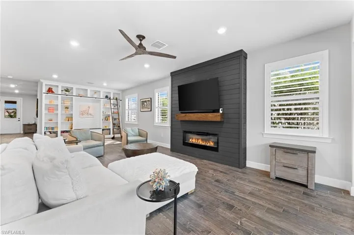 Living room with ceiling fan, a large fireplace, and dark hardwood / wood-style floors