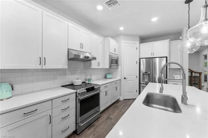 Kitchen with sink, appliances with stainless steel finishes, white cabinetry, dark hardwood / wood-style flooring, and decorative light fixtures