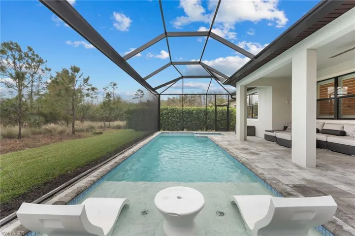View of pool with a patio, outdoor lounge area, glass enclosure, and a lawn