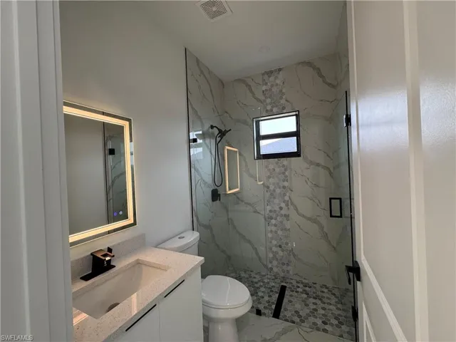 Bathroom featuring a shower with door, vanity, and toilet