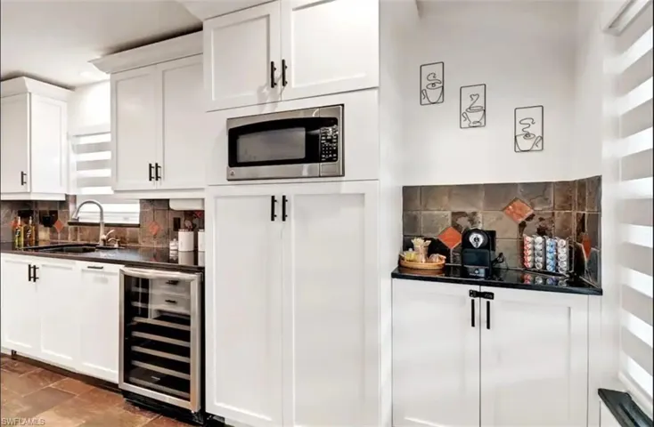 Bar featuring stainless steel microwave, beverage cooler, sink, and white cabinets